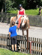 Das Foto zeigt Nikolina auf dem Haflinger Rocky, am Zaun wo auch ein Kind steht.
